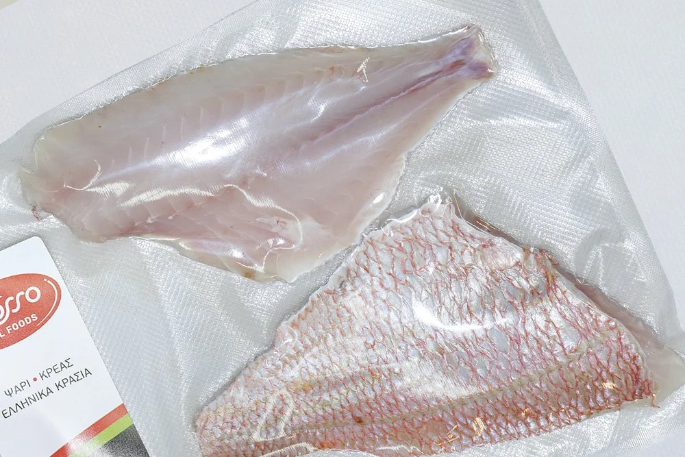 Two pieces of fish fillet in vacuum-sealed packaging on a white surface.