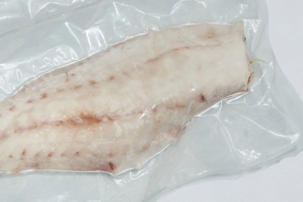 A raw piece of meat, likely bacon, vacuum-sealed in clear plastic packaging.