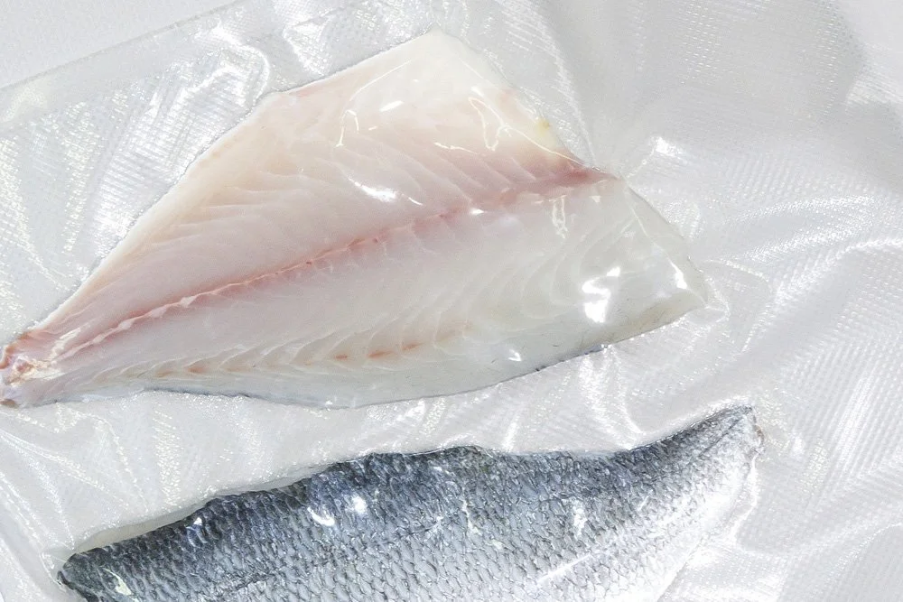 A piece of fish fillet with skin on, placed on a textured plastic surface.