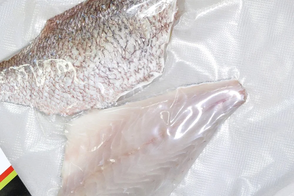 Two pieces of raw fish fillets, one with skin and the other skinless, on a white textured surface.
