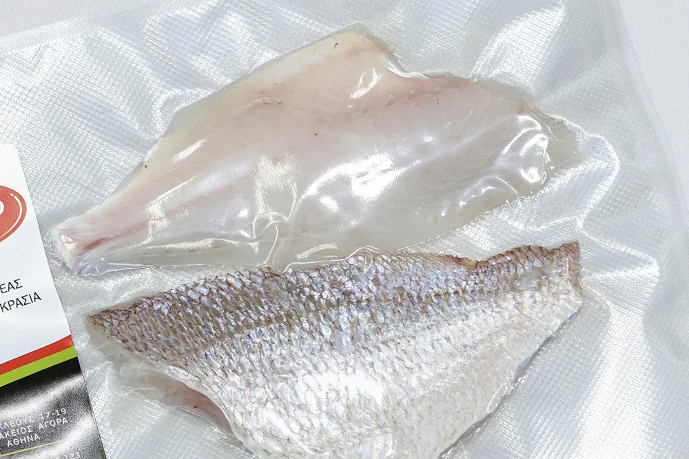 Vacuum-sealed fish fillets, one with skin and one without, on a clear plastic surface.