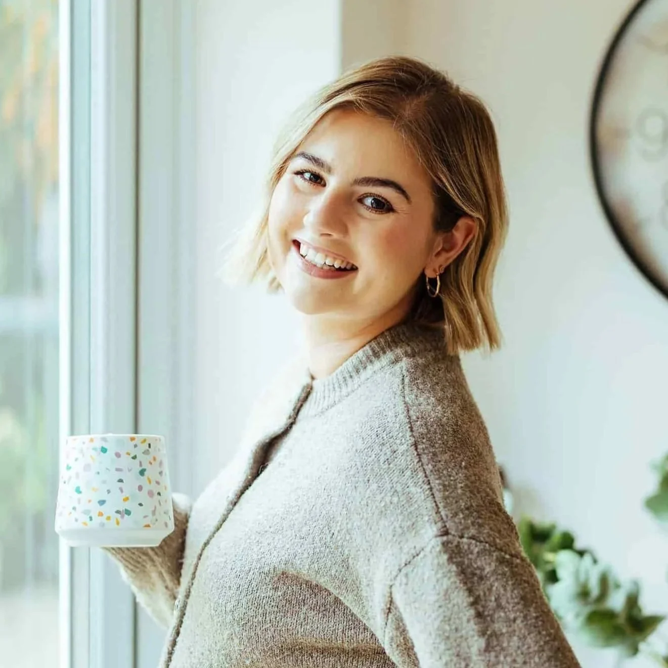 Smiling woman facing the camera wearing a grey cardigan, holding a mug