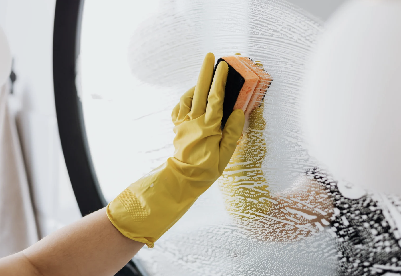 Person wearing yellow rubber gloves cleaning a glass window with a sponge.