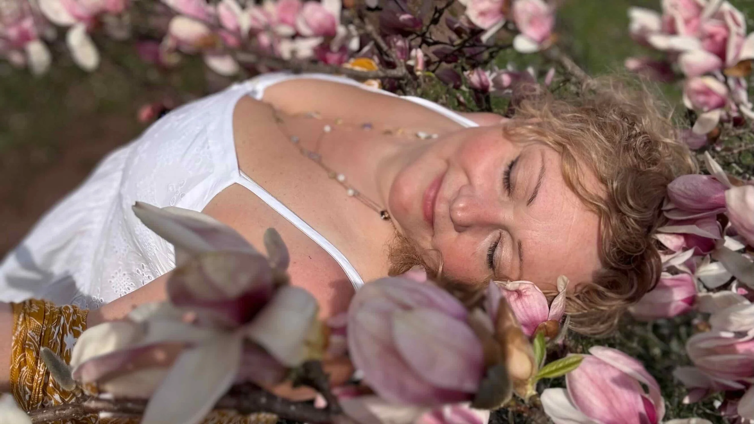 Maya beneath blooming magnolia flowers, symbolizing feminine energy, embodiment, and sacred connection.