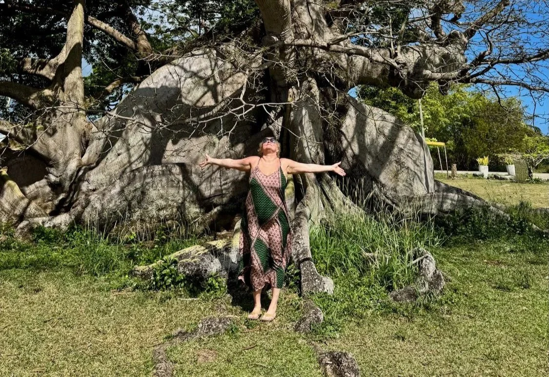 Maya standing beneath an ancient tree, symbolizing grounding, transformation, resilience, and embodied healing through Sacred Love Medicine.