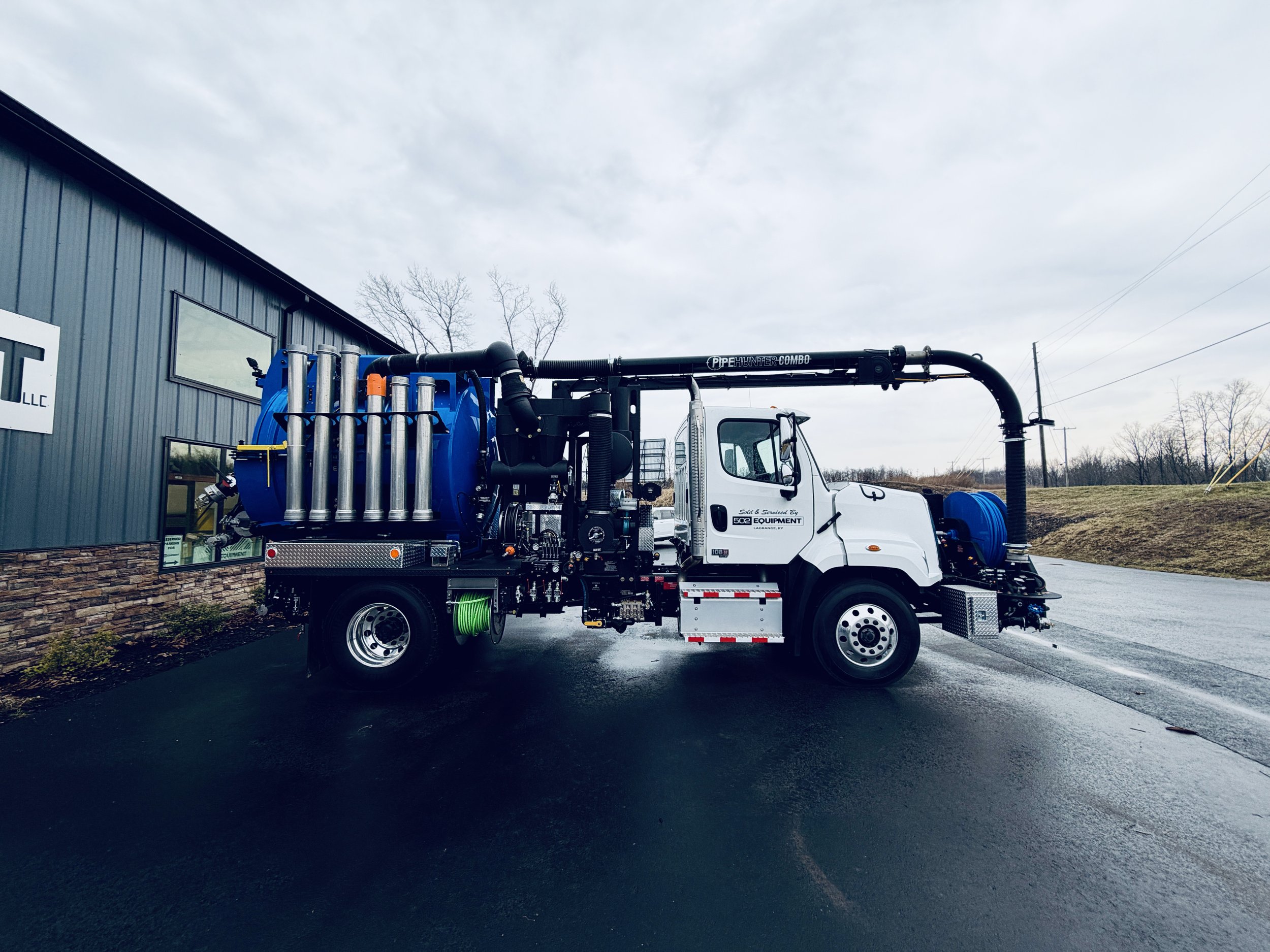 A white and blue industrial vacuum truck parked outside the 502 Equipment vac truck service center near Louisville, KY on a cloudy day.