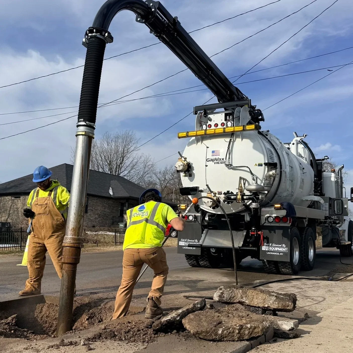 Two construction workers in yellow safety vests and blue helmets working on a street with a GapVax vacuum truck during daytime.