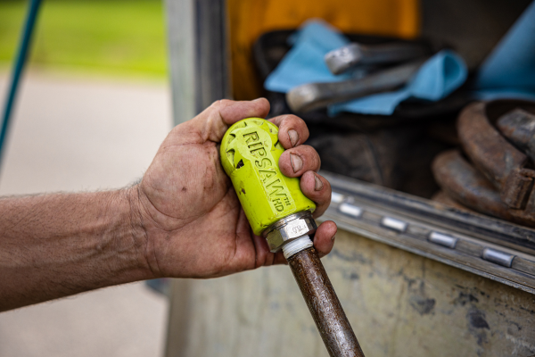 A hand holding a Ripsaw hydro-excavation nozzle connected to a lance.