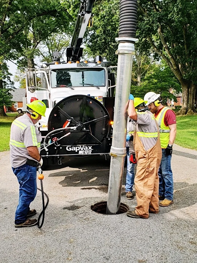 Utility contractors in neon PPE work over a manhold to clean the line using a GapVax vacuum truck sold by 502 Equipment. 
