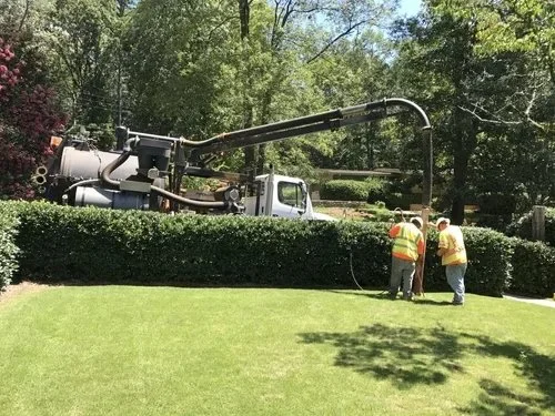 Two workers in yellow safety vests and helmets operating a large vacuum truck on a residential lawn