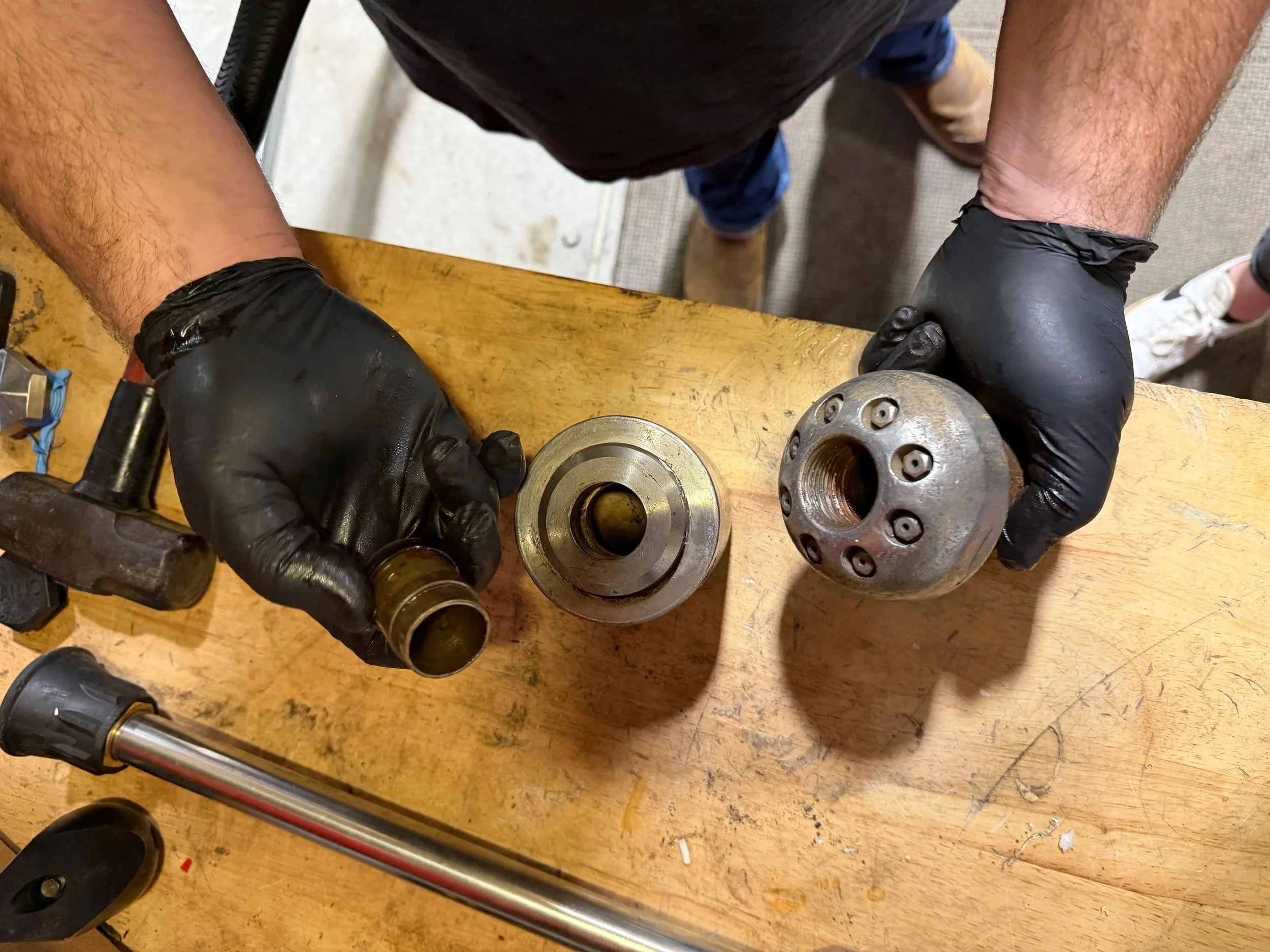 A person wearing black gloves rebuilding a sewer nozzle on wooden workbench at the 502 Equipment nozzle service center in LaGrange, KY.