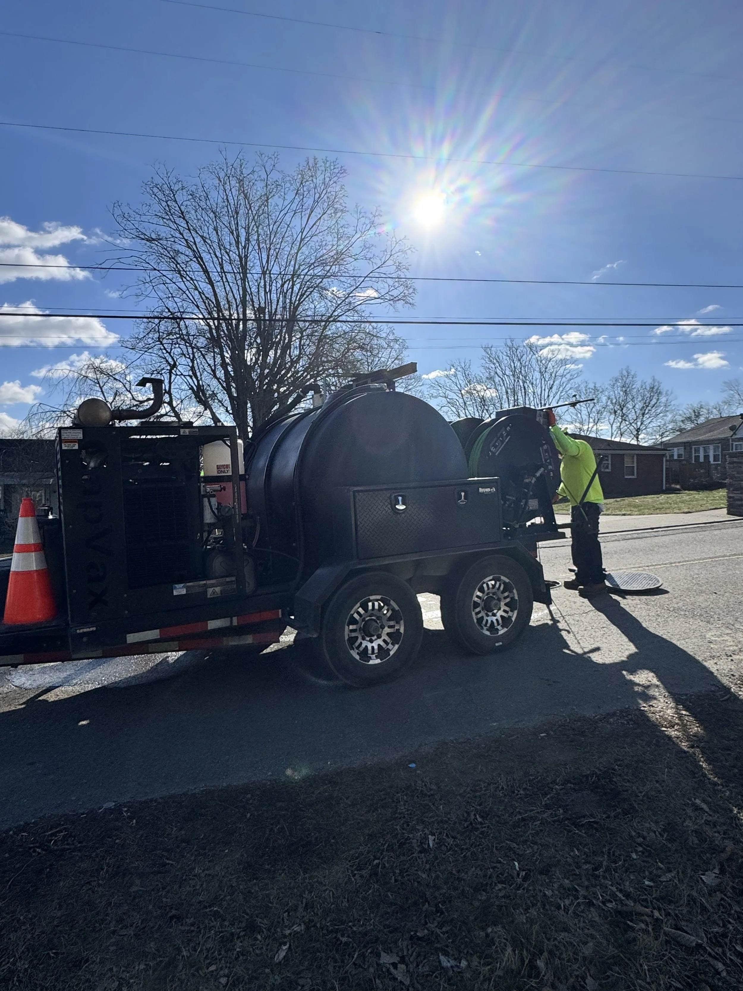 Worker in yellow safety vest jetting pipes with a GapVax g7 trailer jetter on a sunny day with sky and trees in the background.