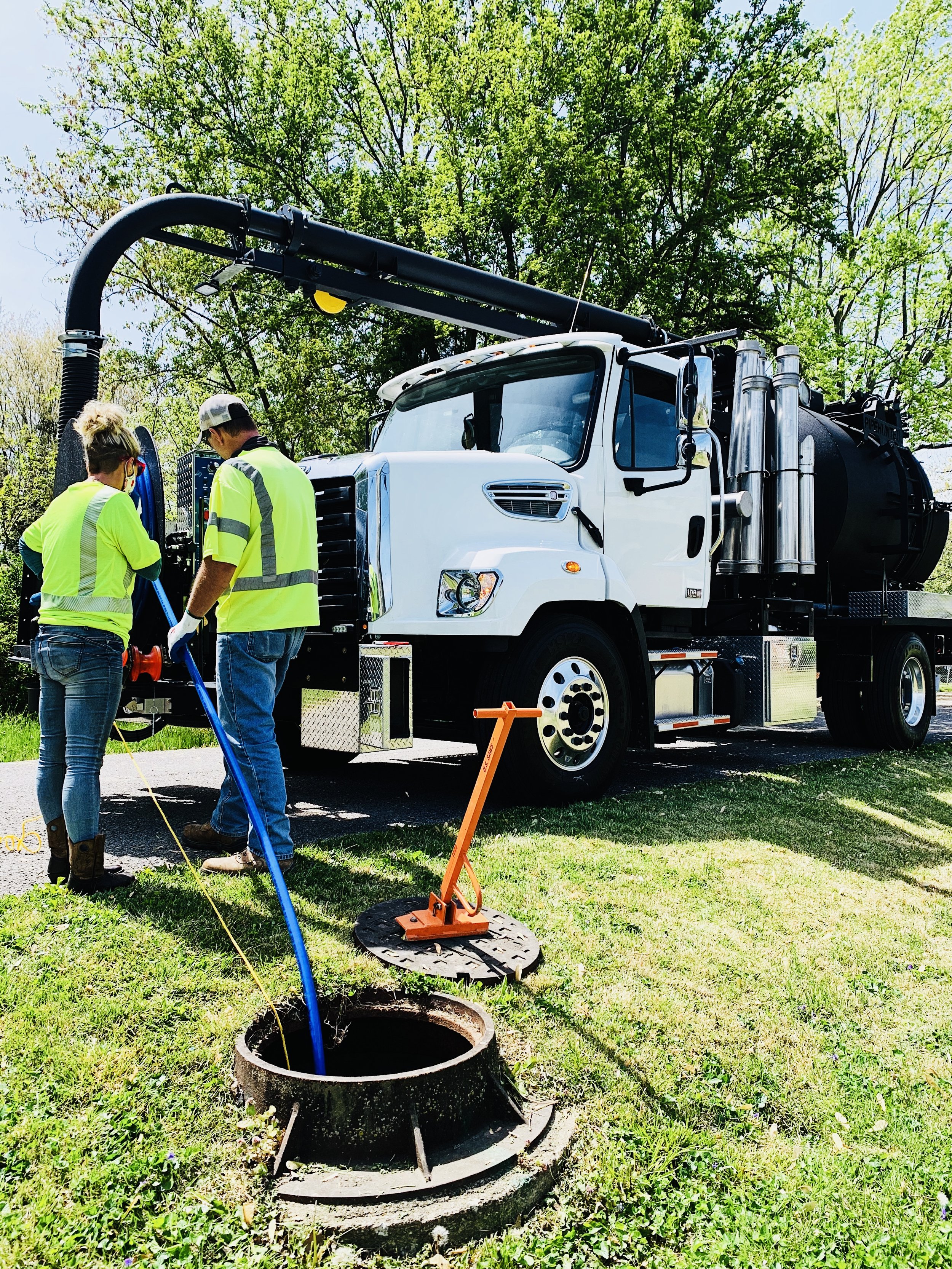 Two workers in safety vests and gloves using a GapVax vacuum truck to clean a sewer pipe. 