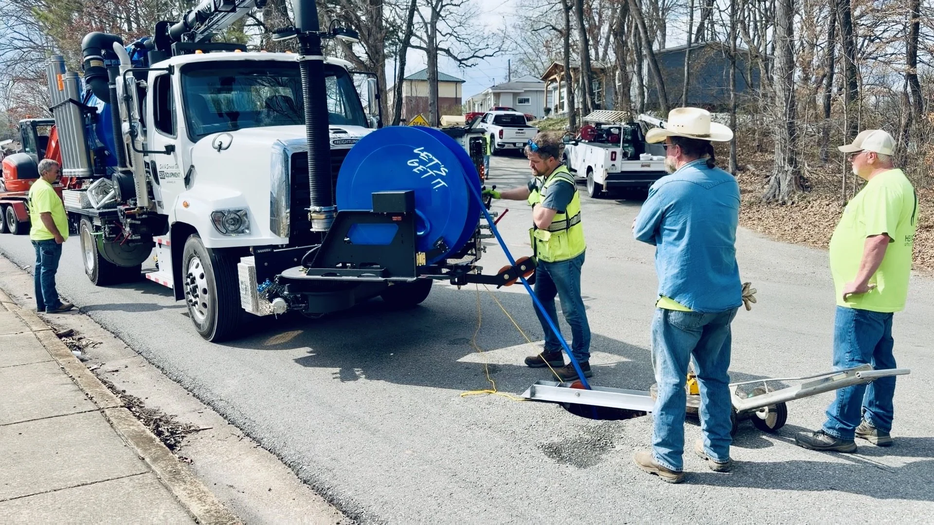 Workers repairing a water leak with a PipeHunter mini combo truck on a residential street.