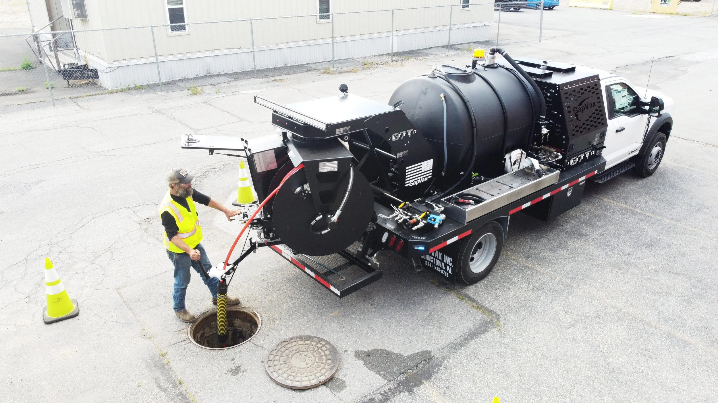 A worker in a yellow safety vest and cap stands outside, operating a GapVax G7T, also known as a high pressure trailer mounted jetter inside a manhole near Lexington, Kentucky.