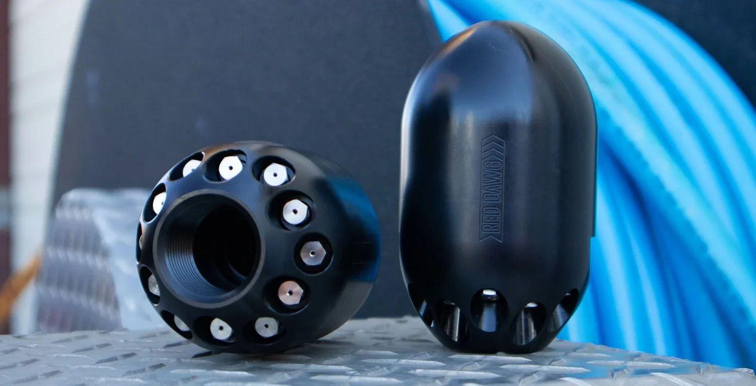 Two black cylindrical objects with multiple holes, placed on a textured surface. One object is lying flat while the other stands upright, with the words 'RED DINGO' visible on the side of the upright object. The background appears iron or metal with a blue hue.