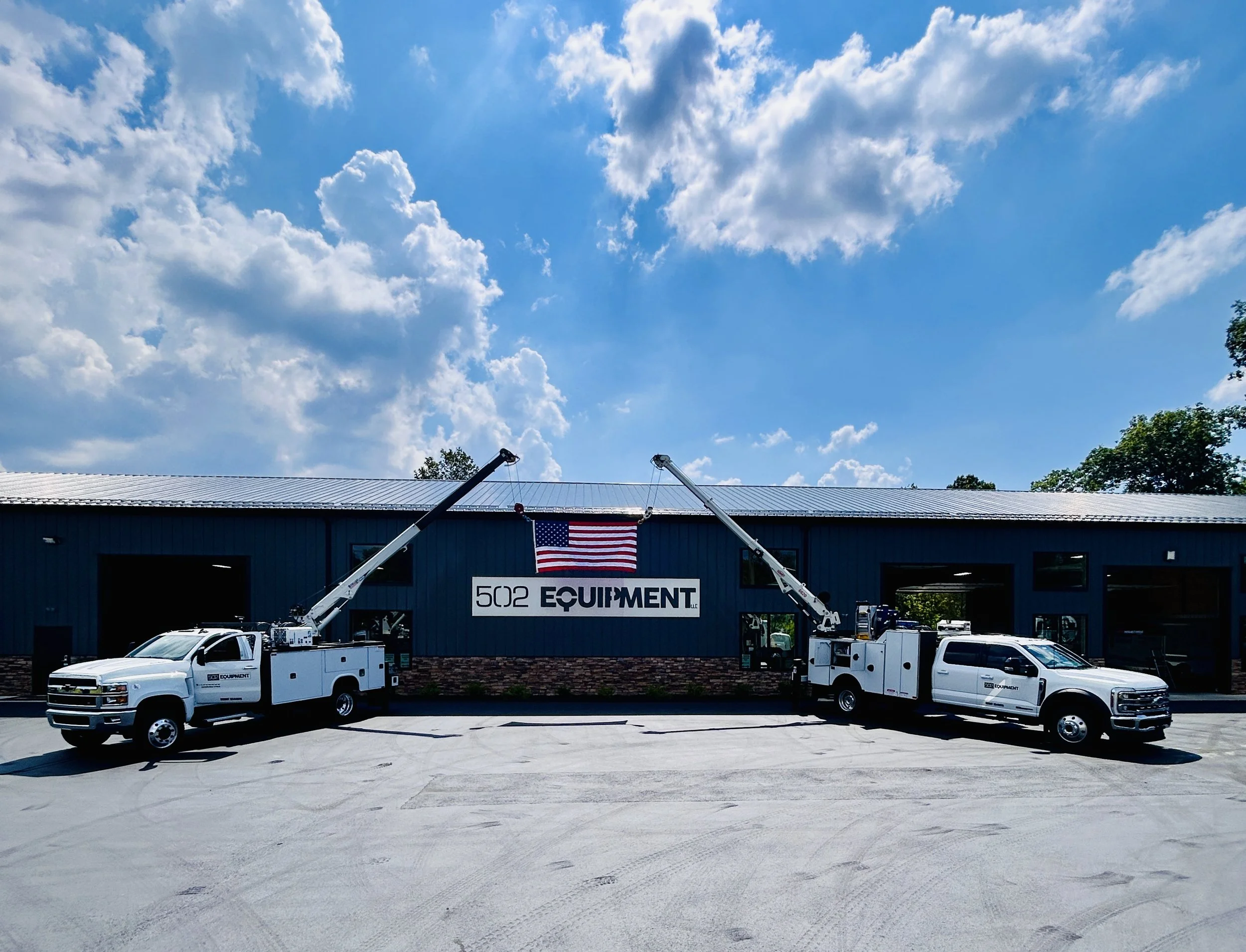 Two mobile service trucks with aerial lifts extend toward large service center in LaGrange, KY with a sign that reads '502 Equipment' and an American flag hanging above.