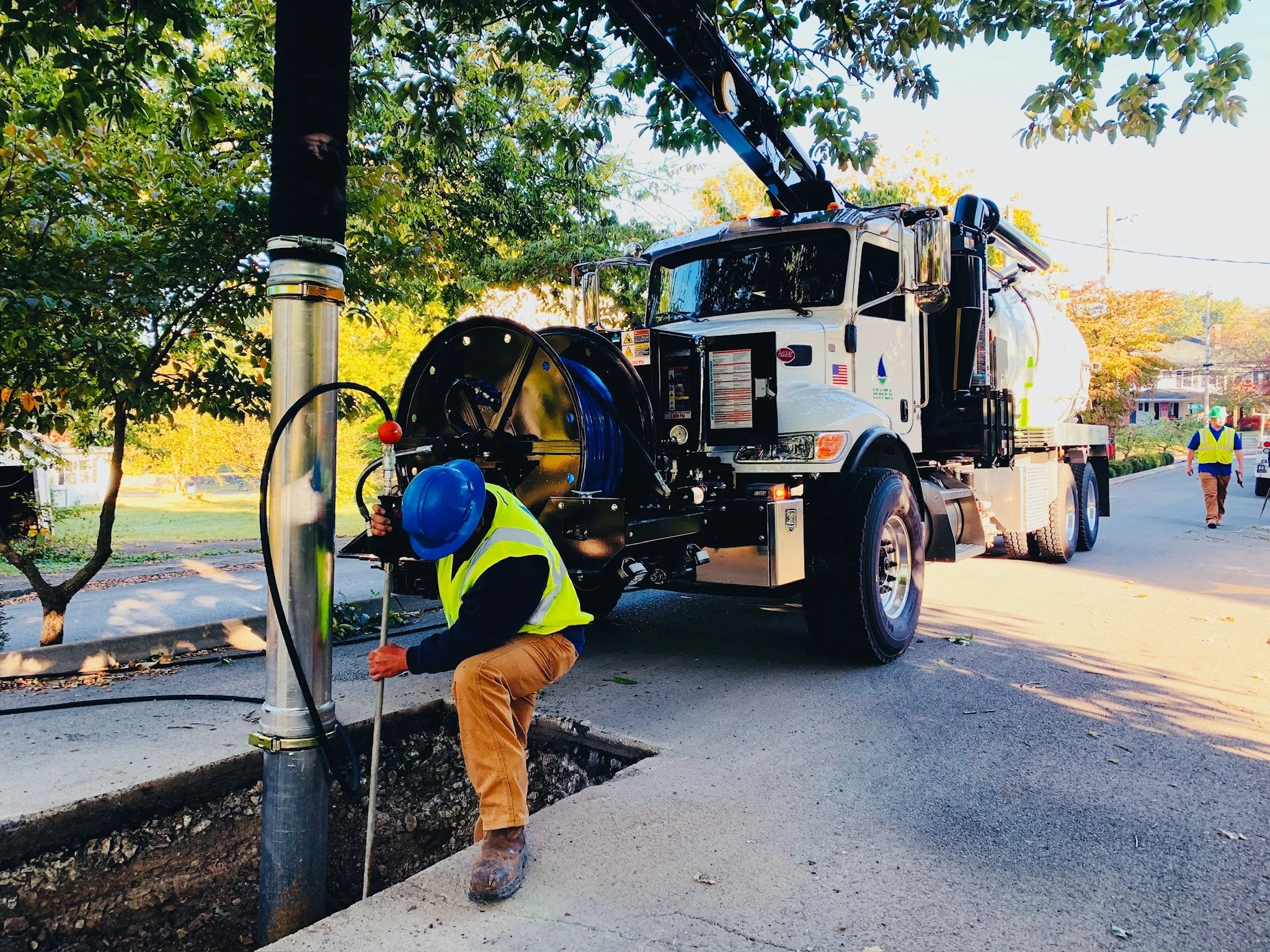 Worker in a yellow safety vest and blue helmet hydro excavating utility line in the street using a GapVax MC vacuum truck. 