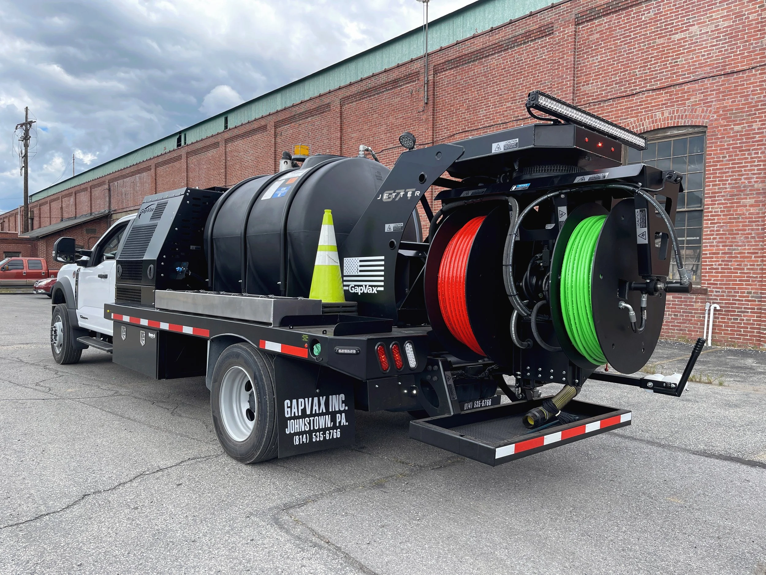 A street cleaning truck with hoses and equipment for cleaning pavements, parked in front of a brick building under cloudy skies.