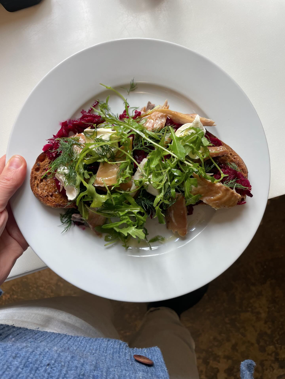 Close-up of a plate with mixed greens salad topped with slices of poultry, greens, beets, and a piece of toasted bread.