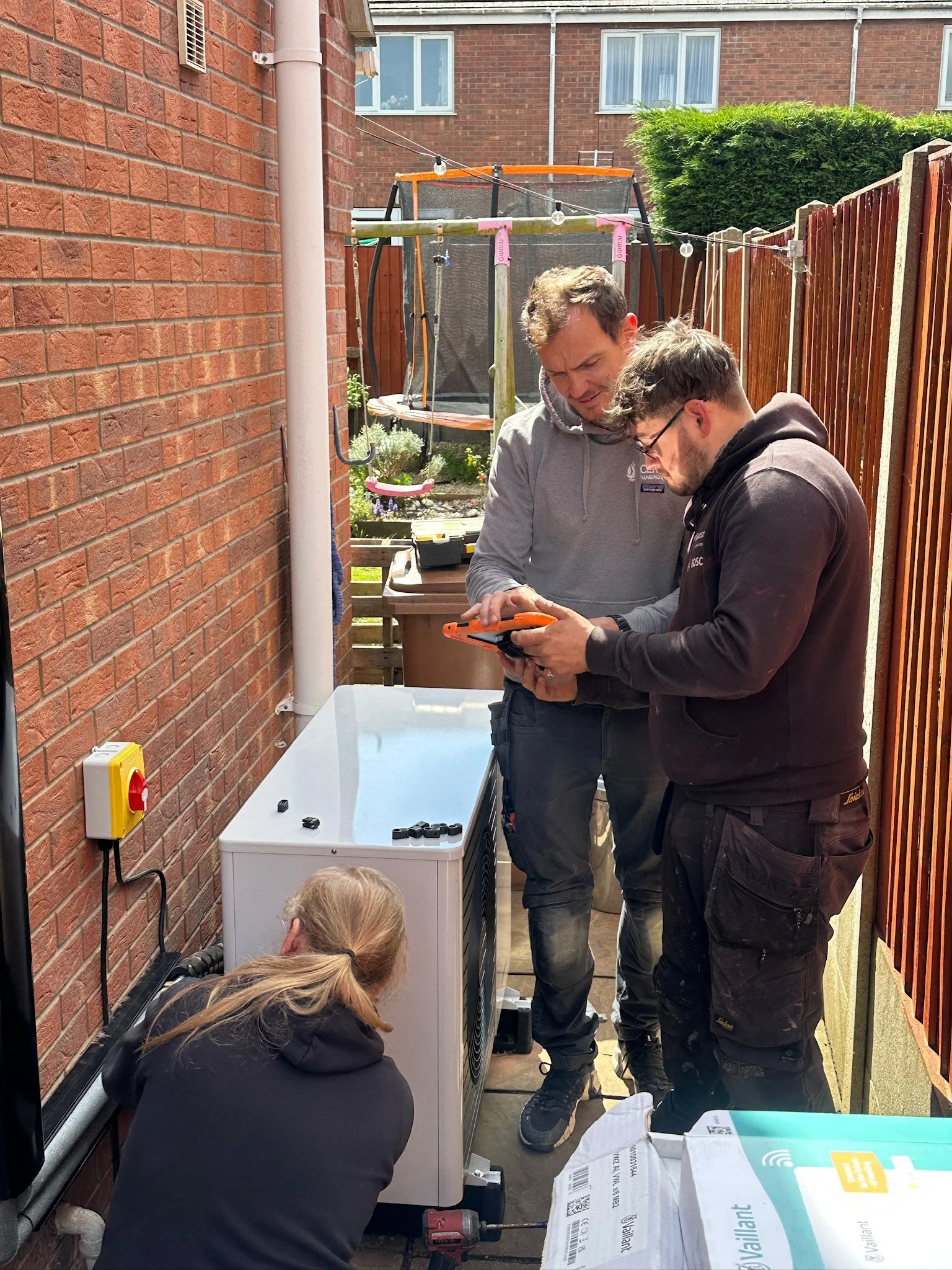 Lincoln heat pumps team commissioning a vaillant arotherm plus heat pump. 2 team members are looking an ipad, one engineer is fitting cable clips.