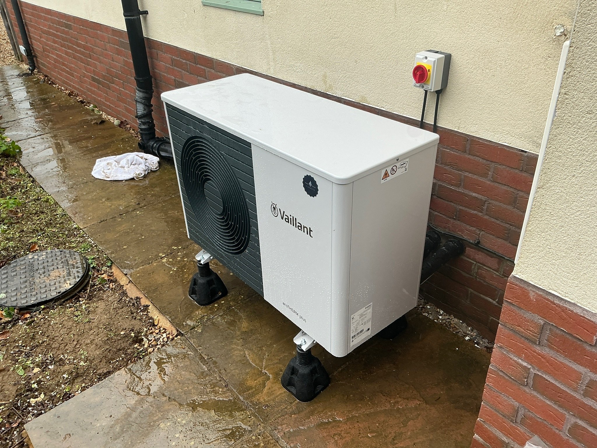 Vaillant arotherm plus 5KW heat pump. Heat geek installation with heat geek guarantee sticker. the heat pump is installed on adjustable rubber feet. it has been raining. The electrical rotary isolator is above the heat pump.