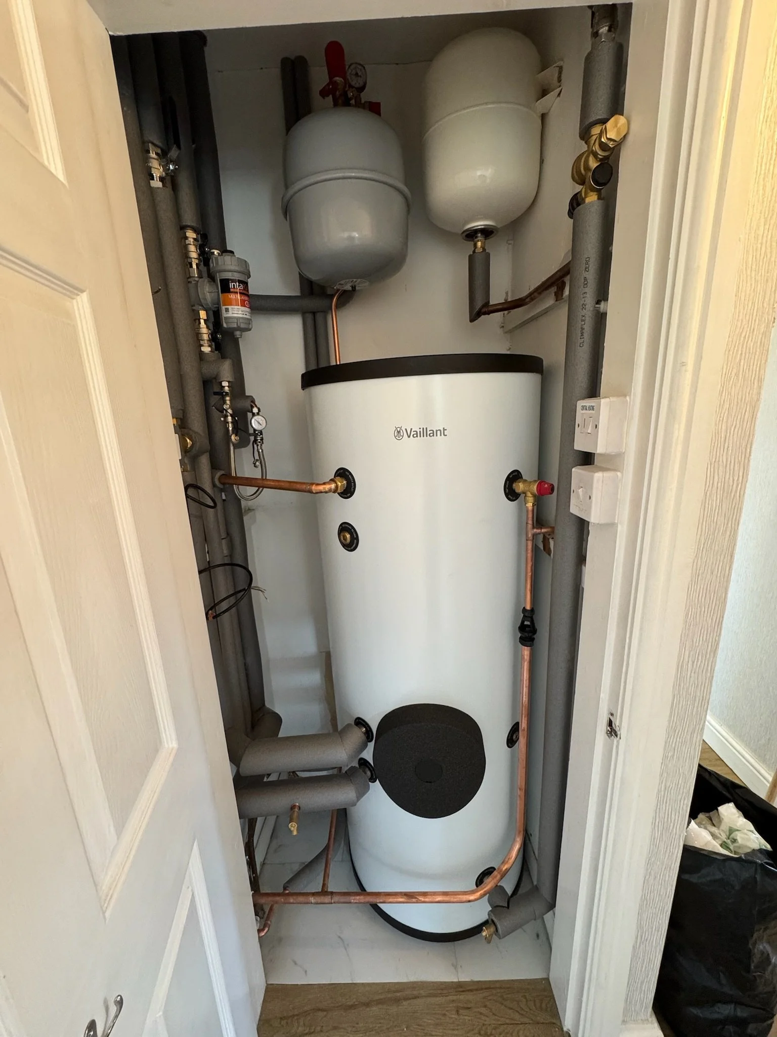 Vaillant Pure 210 litre unvented cylinder installed in an airing cupboard. Pipework is insulated and neat. you can see the intaklean filter, 2 expansion vessels and filling loop with pressure gauge.