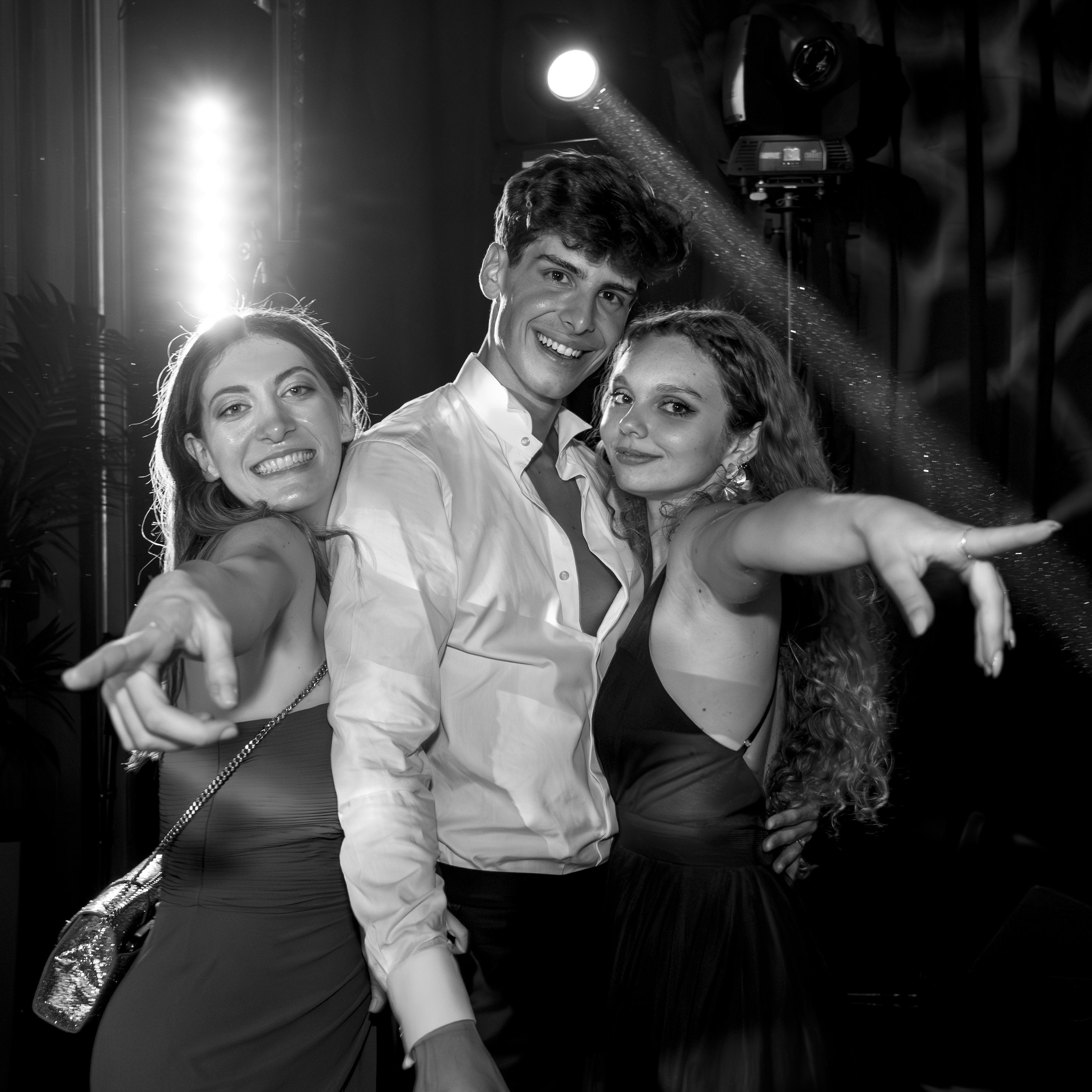 Trois jeunes adultes souriants posant pour une photo dans une boîte de nuit, en noir et blanc.