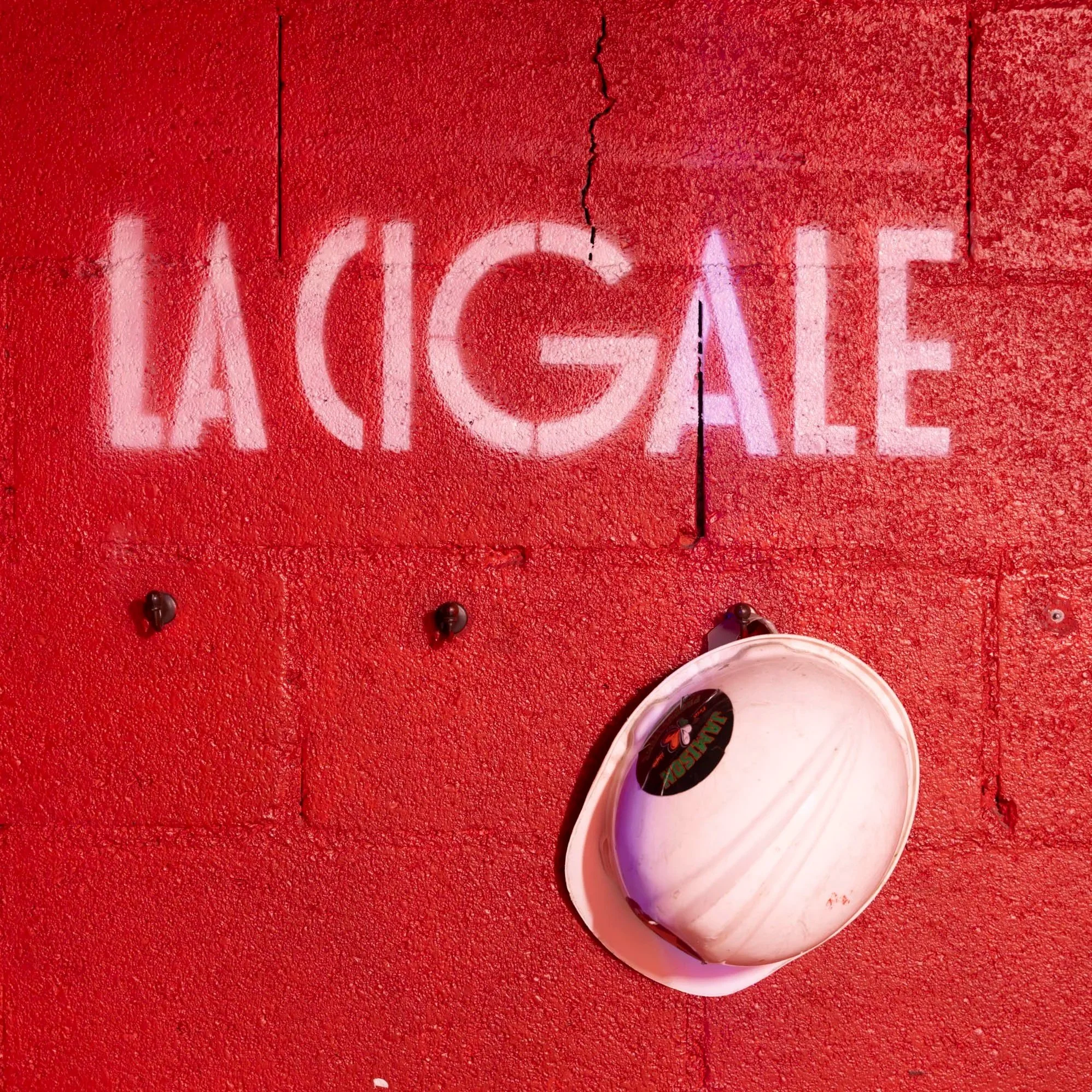 Une enseigne lumineuse indiquant 'LAIGE' sur un mur rouge, avec une casquette blanche suspendue devant le mur.