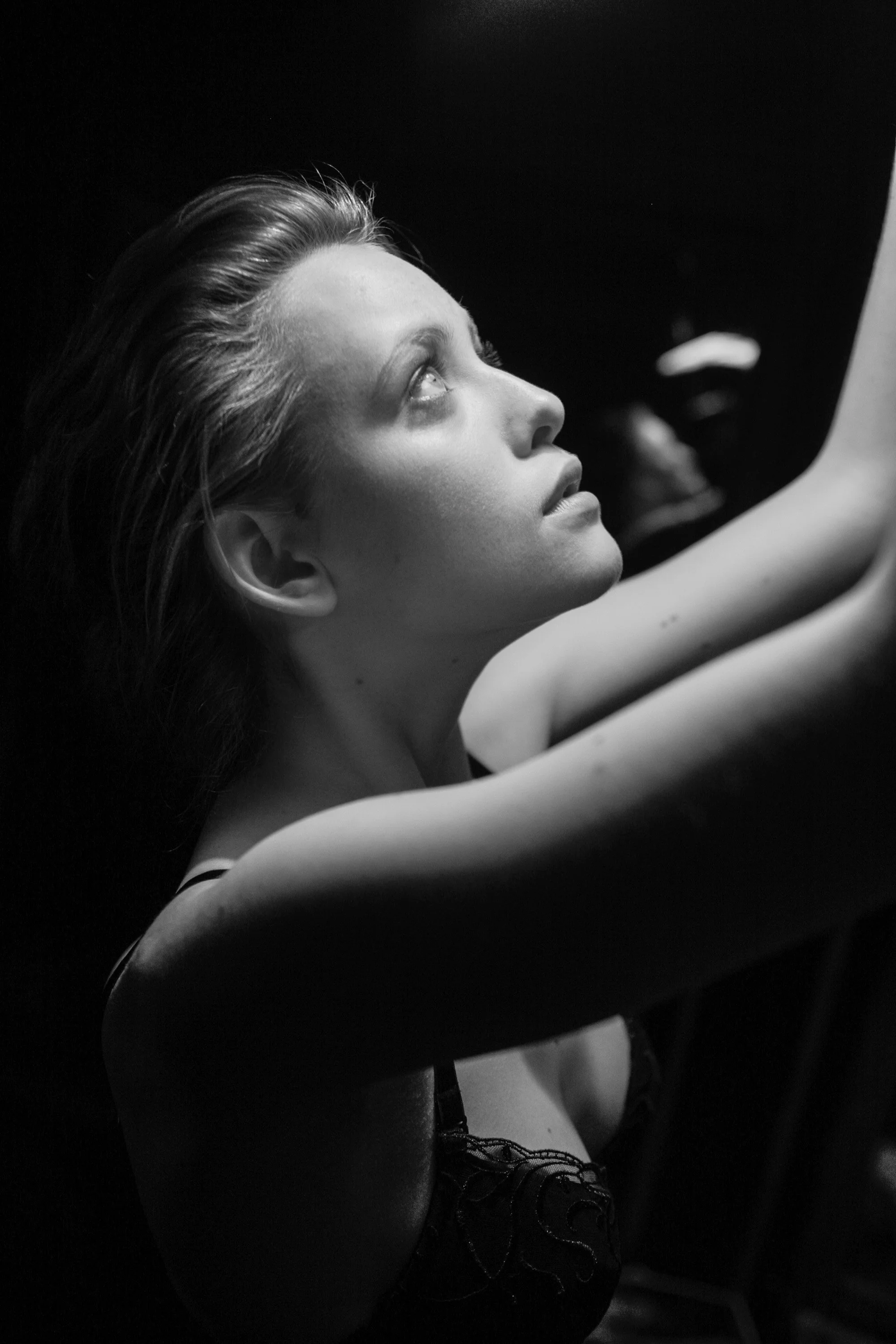 Portrait en noir et blanc d'une jeune femme regardant vers le haut, bras levés, expression contemplative