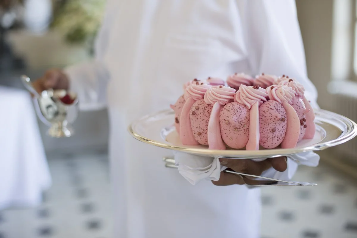 Gâteau rose décoré de crème et de petits éléments décoratifs, présenté sur un plateau argenté