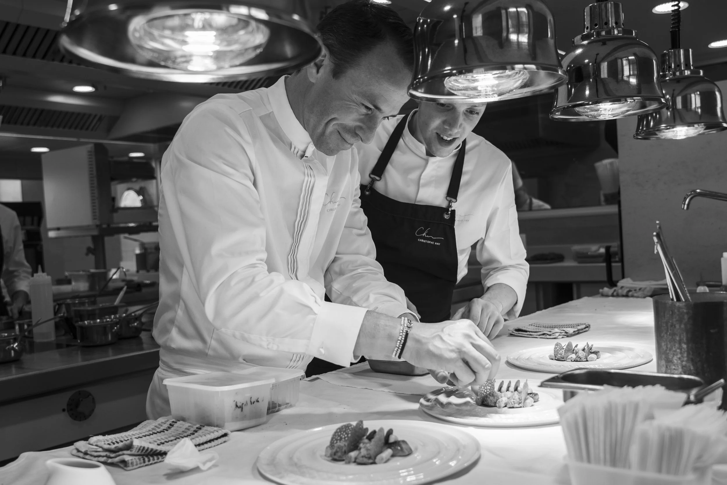 Deux chefs en uniforme décorent des assiettes de desserts dans une cuisine professionnelle.