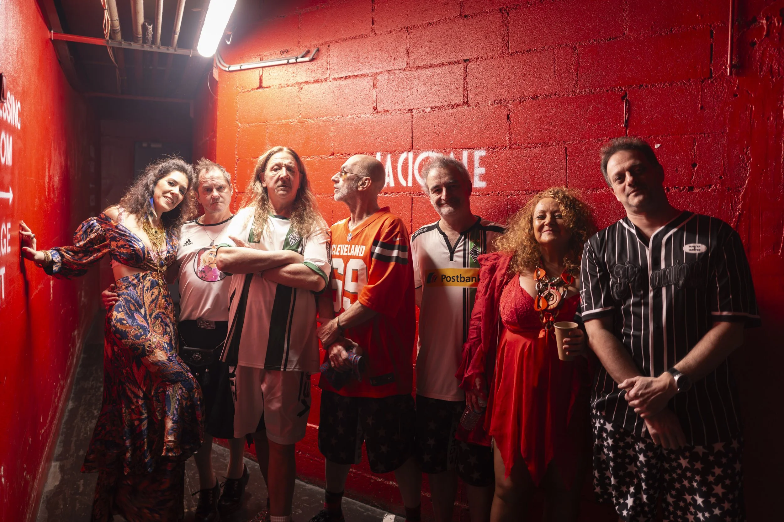 Groupe de sept personnes posant dans un couloir rouge, certains portant des maillots de football.