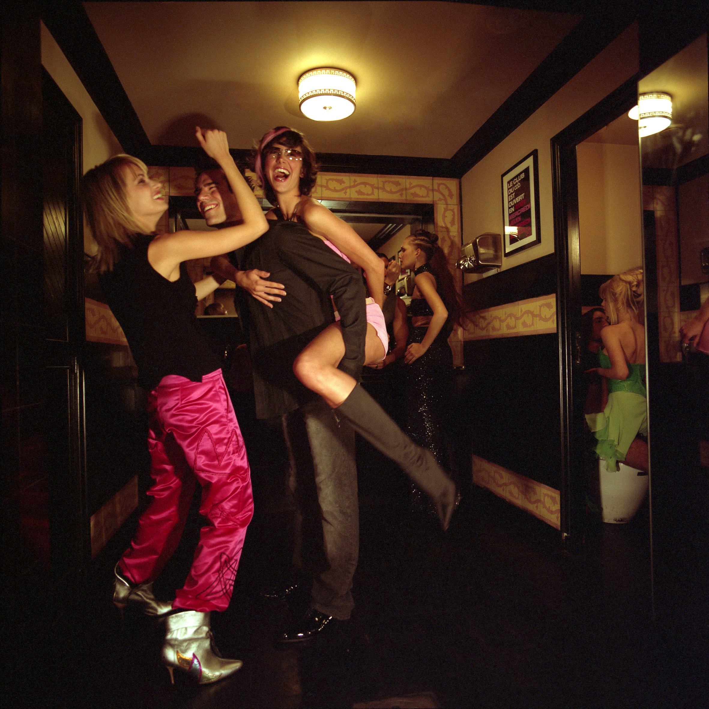 Groupe de jeunes danseurs dans une soirée festive, avec une femme en haut d'une autre, tous souriant et s'amusant.
