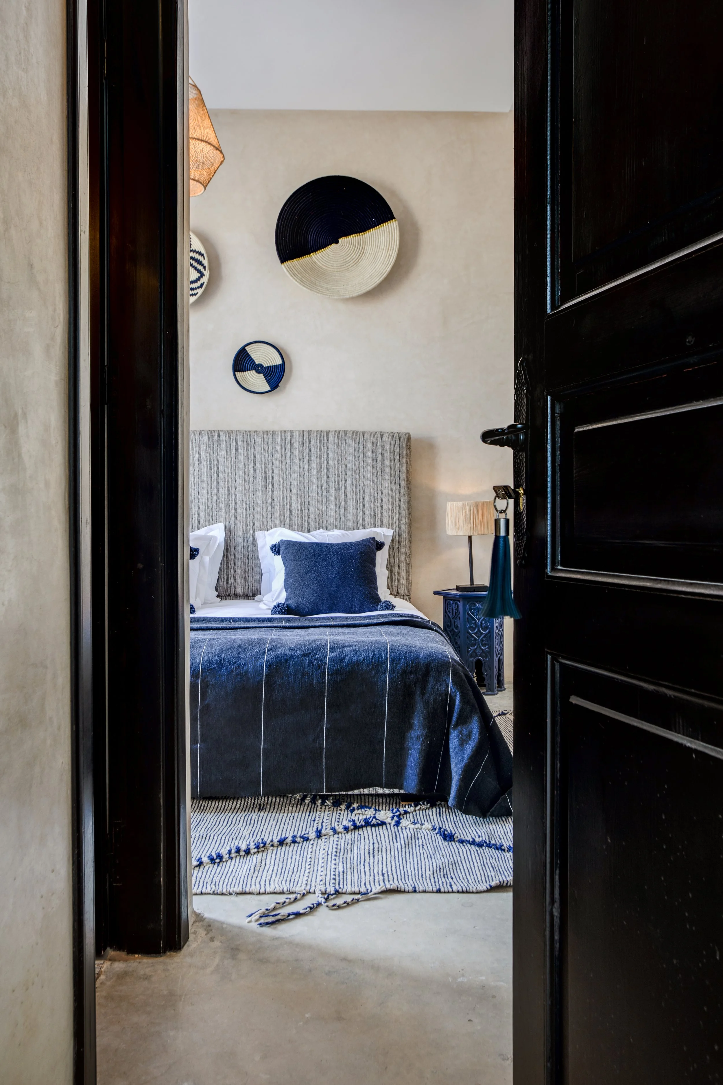 Chambre avec un lit à tête de lit rayée, décorations murales en forme de cercles noirs, blancs et bleus, une table de chevet bleue avec une lampe beige et une tête de lit grise.