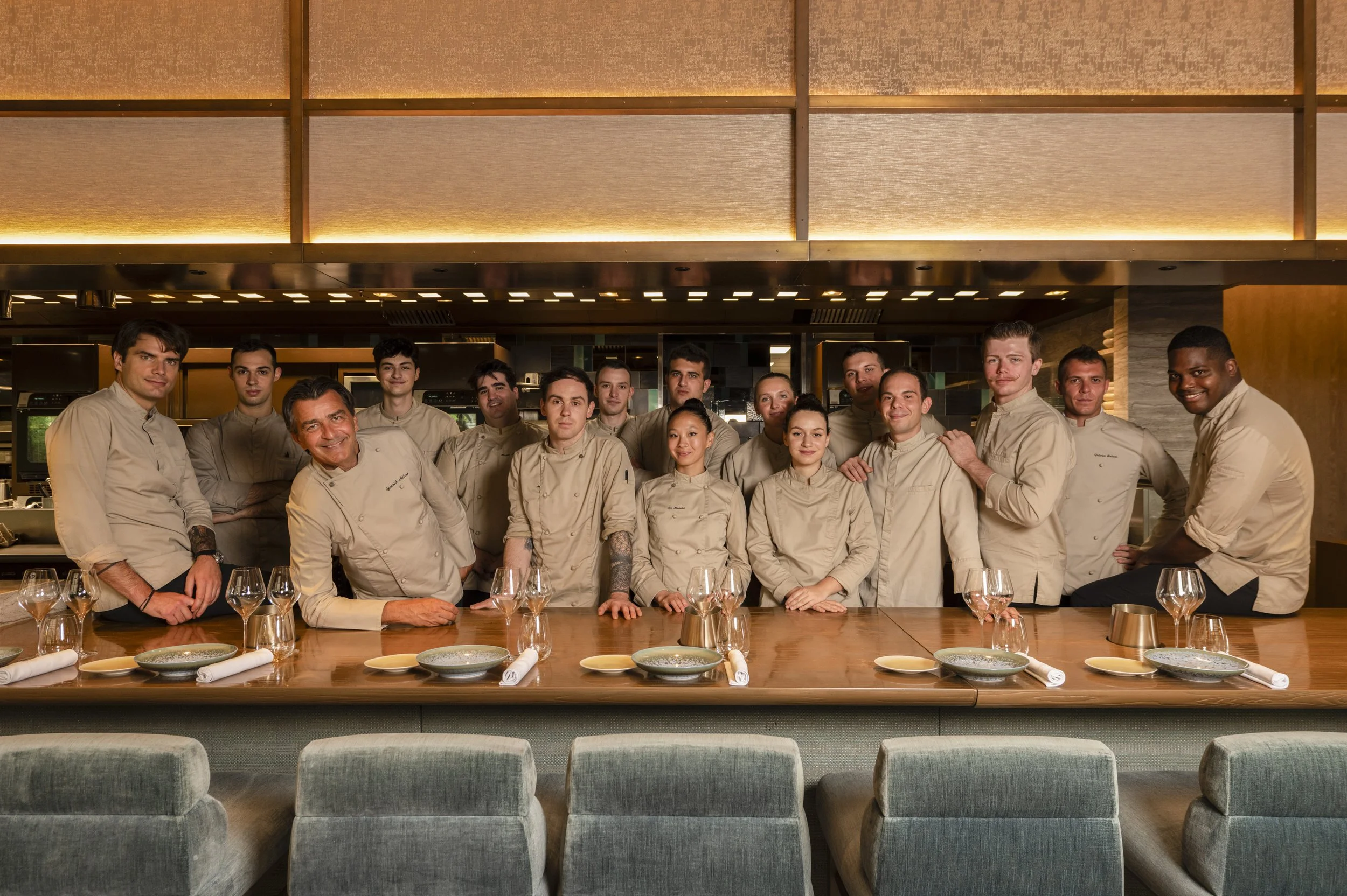 Groupe de chefs de cuisine posant dans une cuisine d'un restaurant, certains souriant, avec une table dressée devant eux.