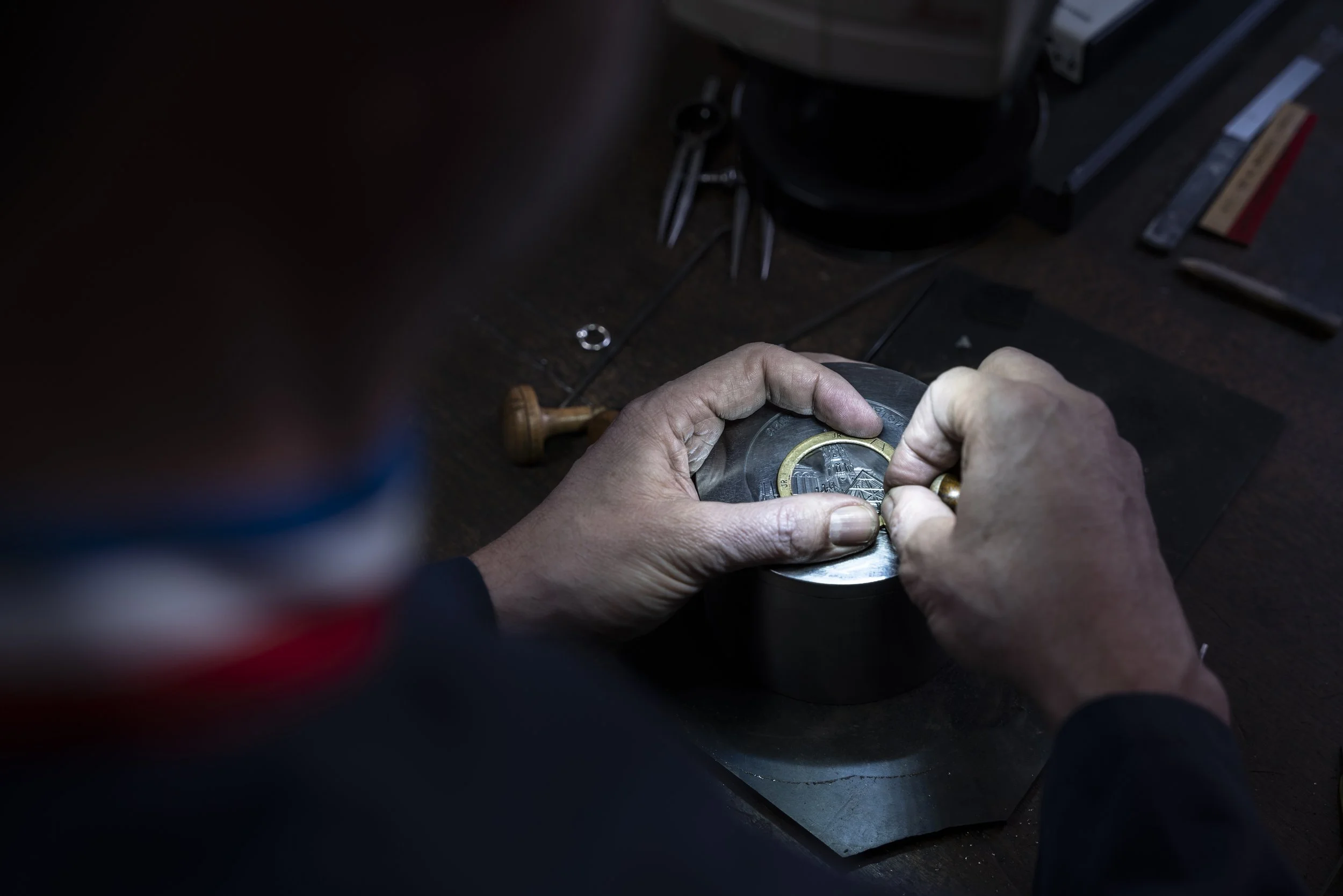 Un artisan travaille sur une pièce de monnaie près de ses outils sur un établi en bois.