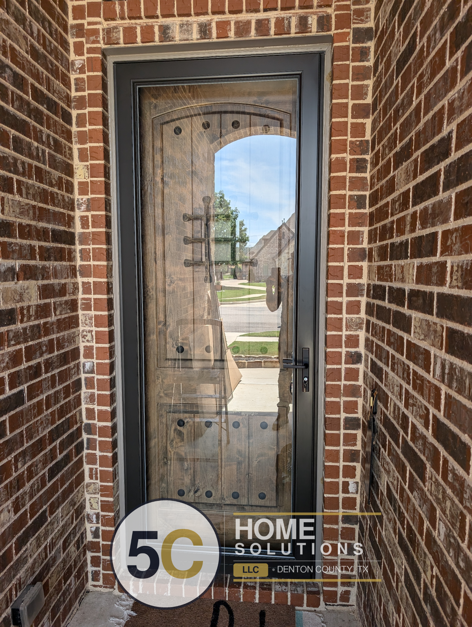 Storm door installation on rustic wood front door with black frame and full glass panel - Handyman Services Denton TX