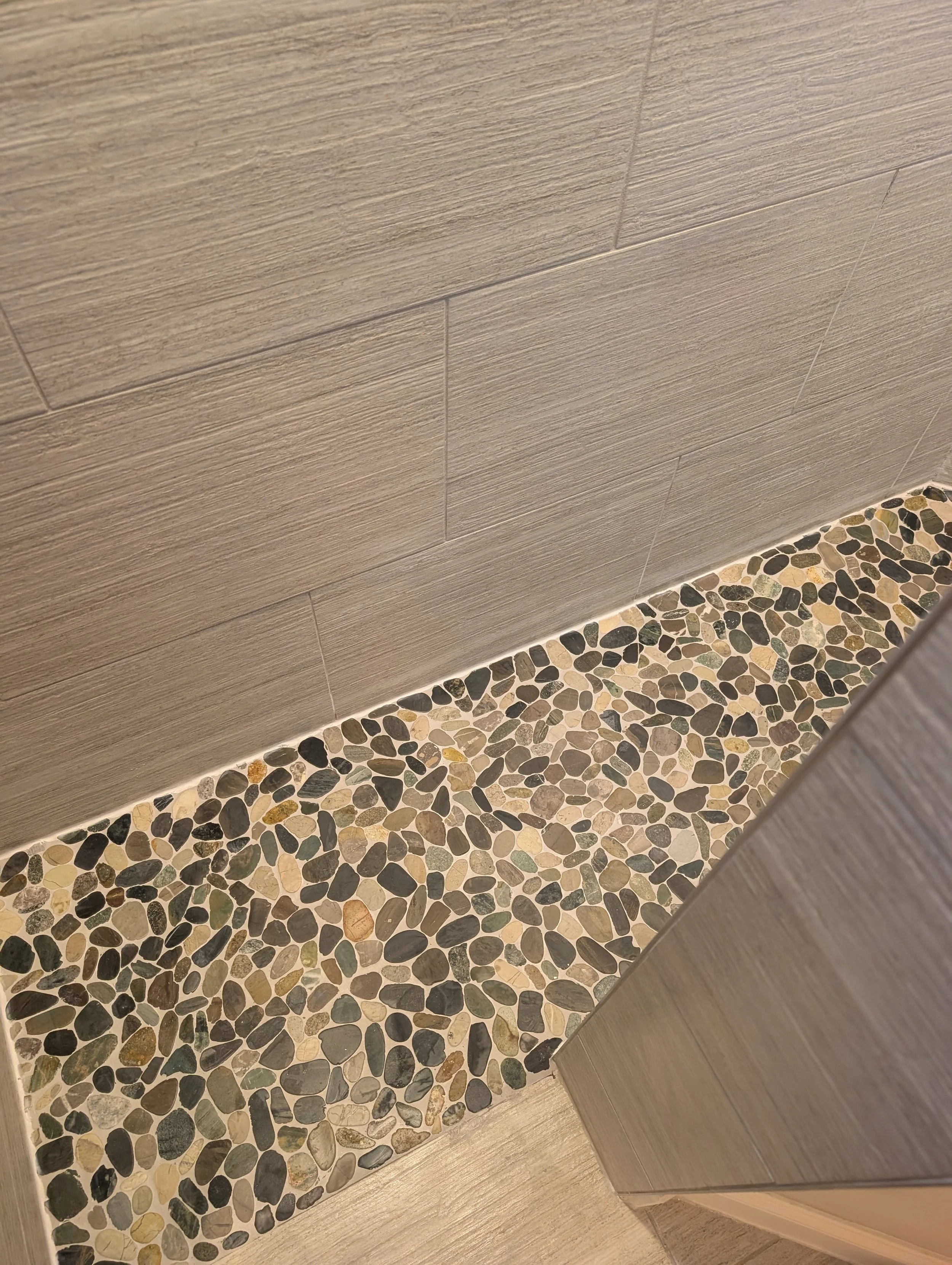 Close-up of a pebble stone shower threshold in Denton County, TX. Seamless tile transition with precision edge work and expert grouting.