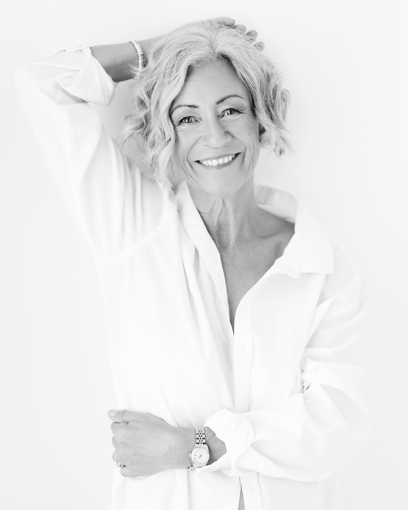 women over 60 leaning on wall in white shirt smiling whilst being photographed in portrait studio shropshire