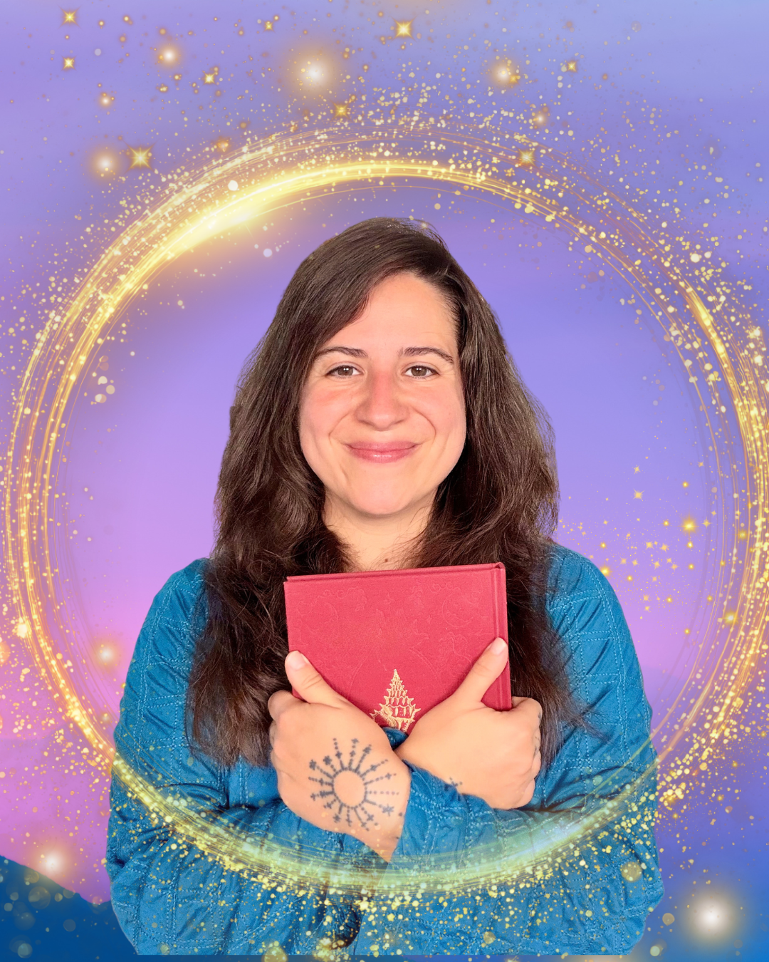 Woman with long dark hair, smiling, holding a red holiday-themed card, standing in front of a purple background with glowing golden sparkles and swirling light effects, wearing a blue patterned shirt, and has a tattoo of a snowflake on her hand.