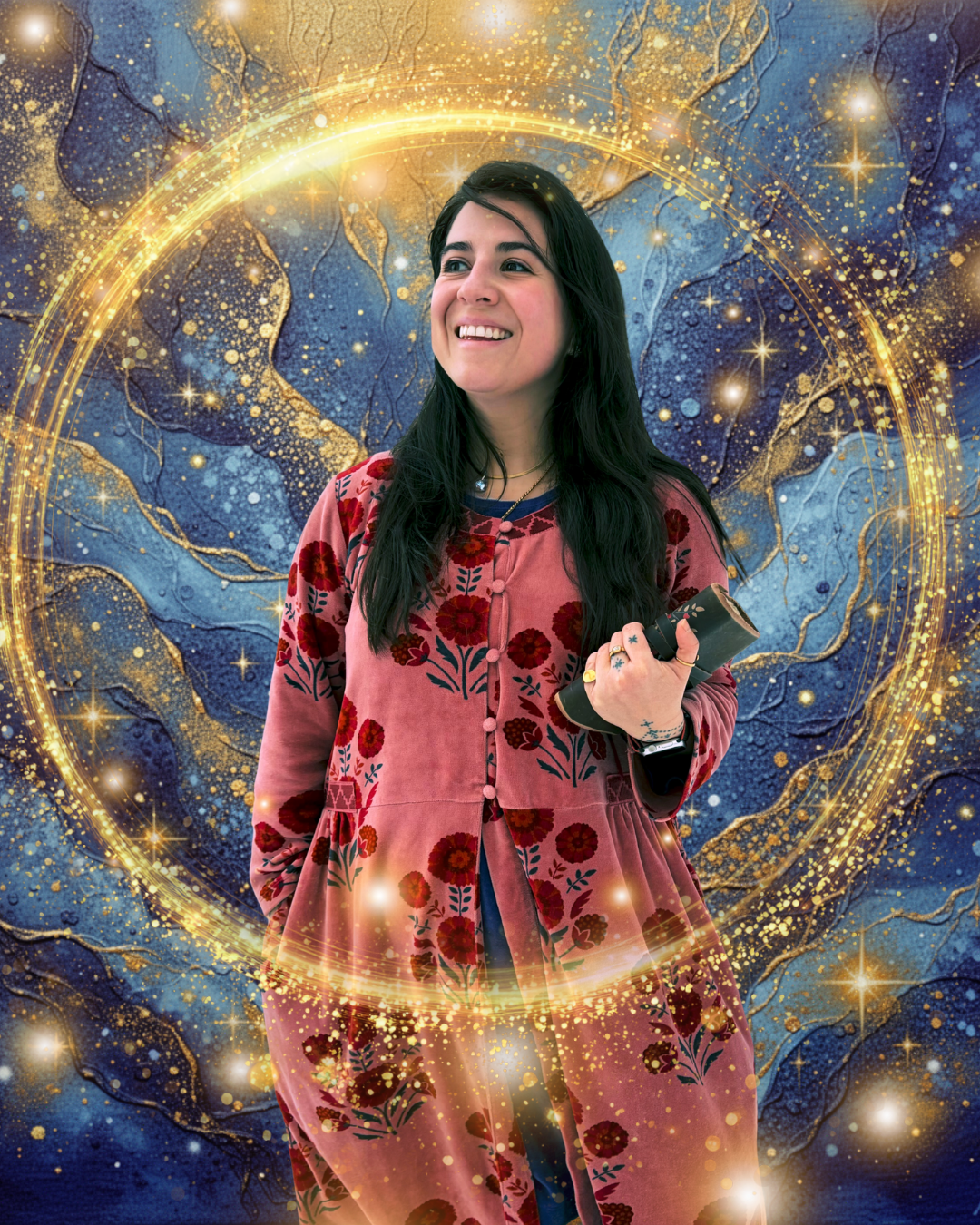 A woman with long dark hair wearing a pink floral dress, smiling and holding a black device, standing in front of a cosmic background with gold glowing rings and star patterns.