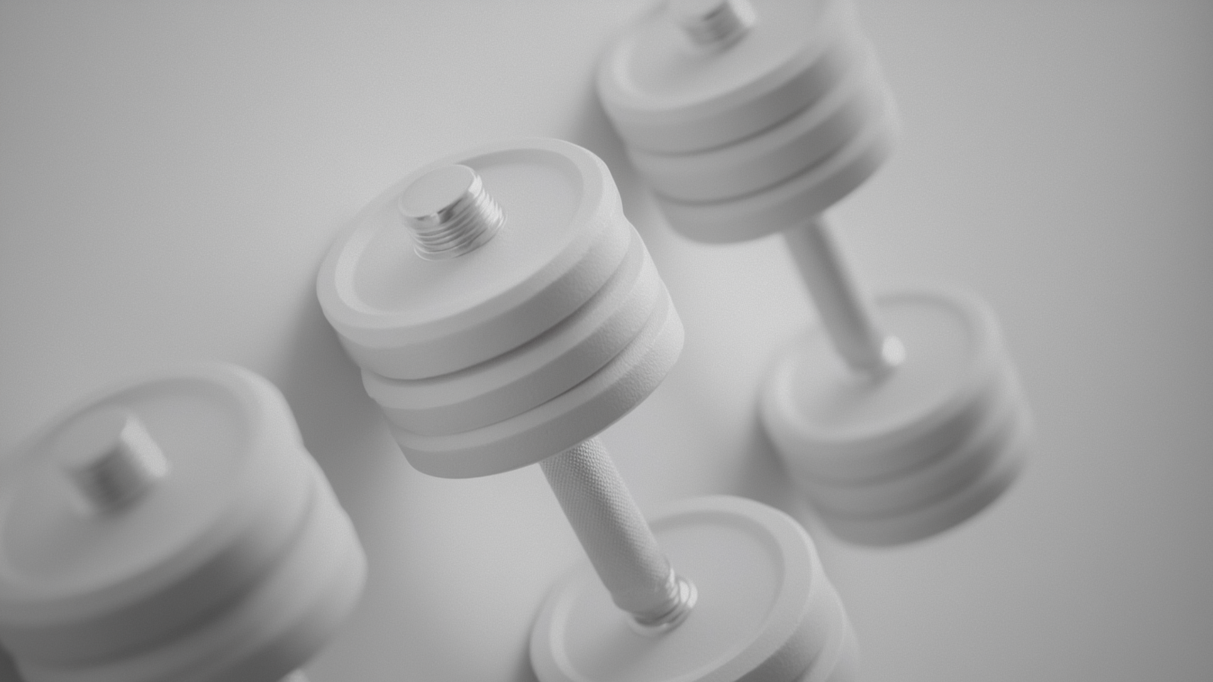 A close-up of two adjustable dumbbells with white weight plates and textured handles, set on a light-colored surface.
