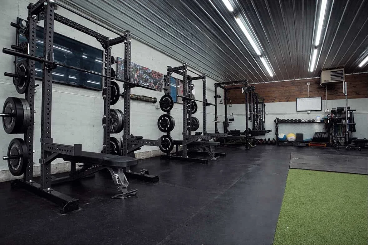 Empty grand forks gym with black weightlifting racks, barbells, weight plates, medicine balls, and kettlebells on shelves.