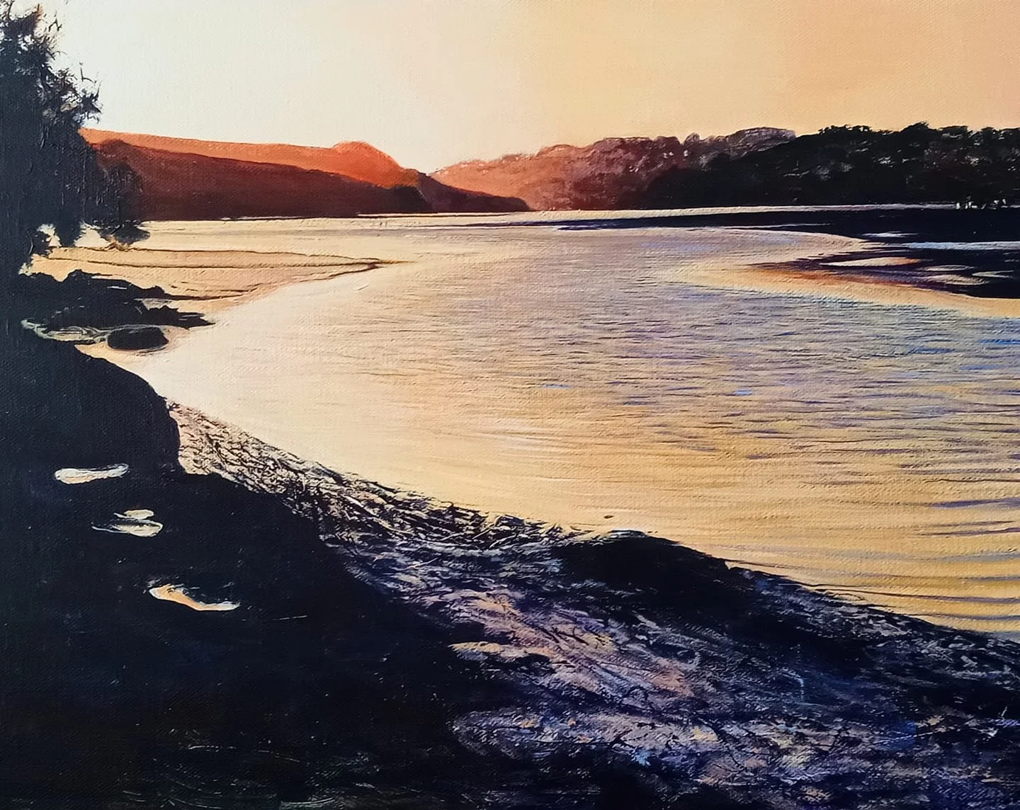 Sunset over a calm river with gentle waves, rocky shoreline, and silhouetted trees and hills in the background.