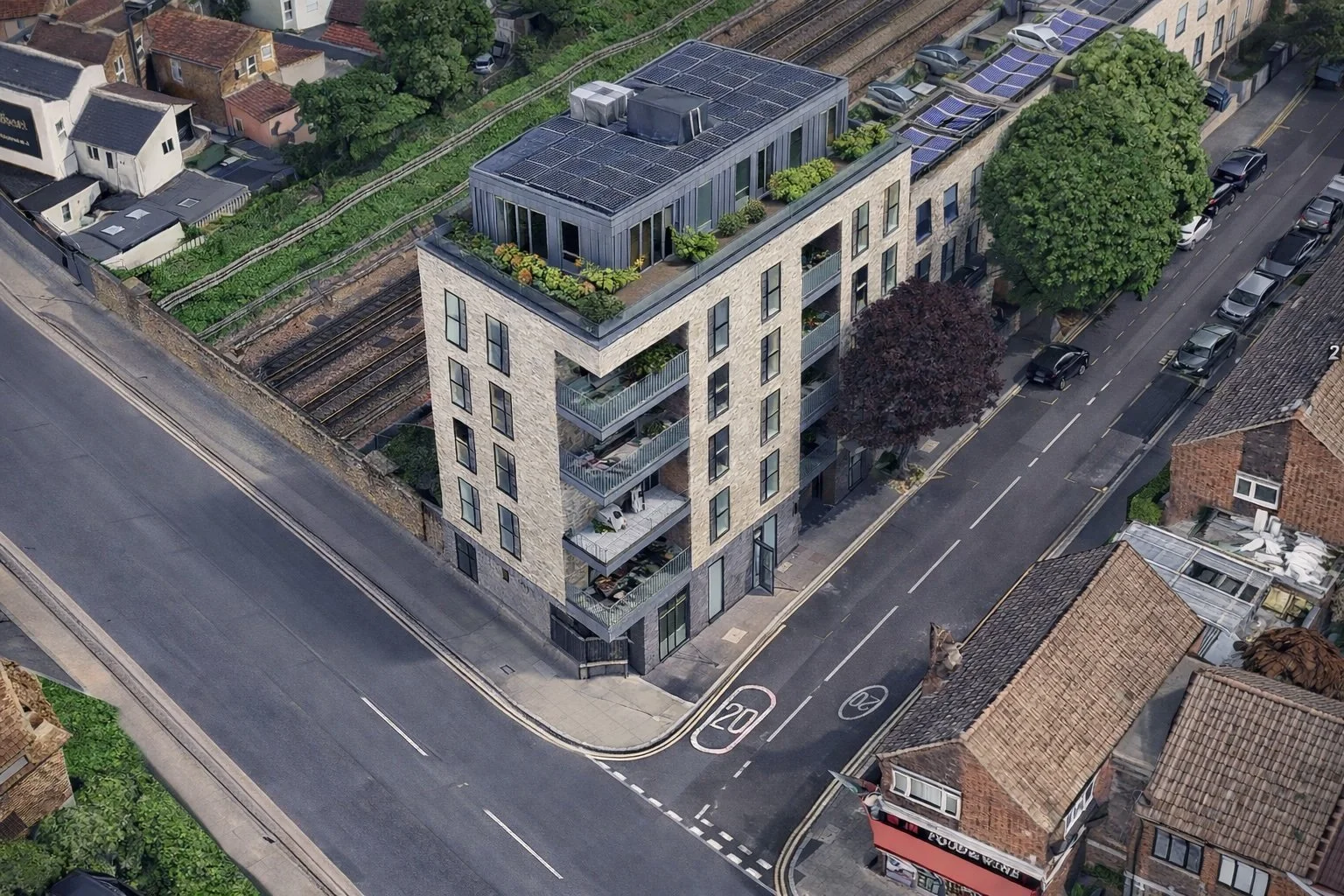 An aerial view of a modern multi-story apartment building with balconies and rooftop garden, situated on a city street corner surrounded by other residential buildings, with parked cars along the street.