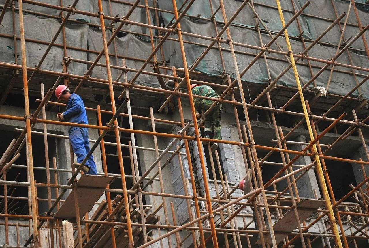 Construction workers in safety helmets working on a building surrounded by orange scaffolding.