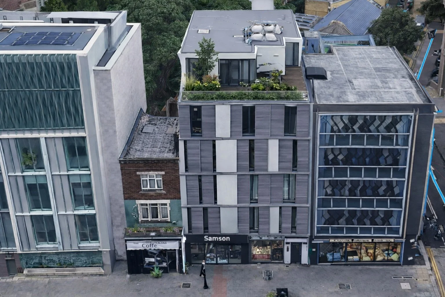 Aerial view of a city street with modern buildings, storefronts, and a person walking on the sidewalk.