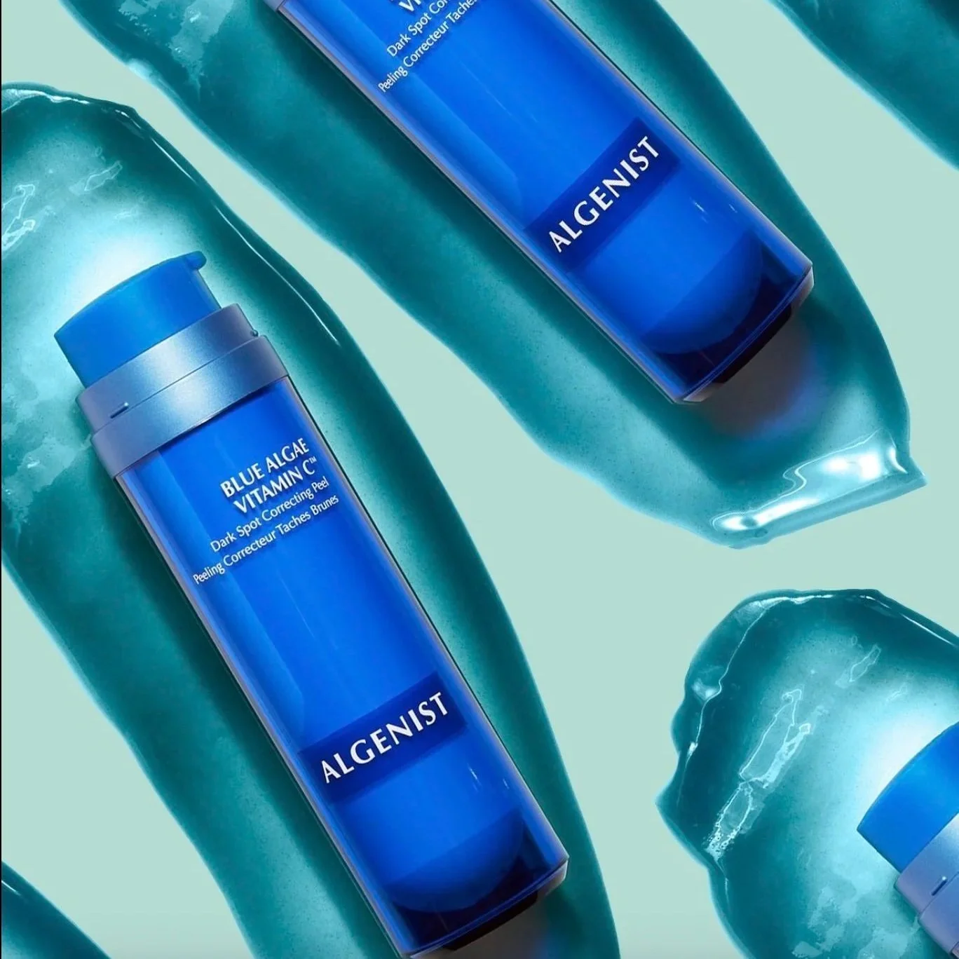 Multiple ALGENIST Blue Algae Vitamin C skincare bottles on top of a gel-like substance on a light green background.