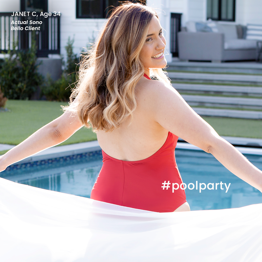 Smiling woman modeling in a red swimsuit with long, wavy hair standing by a pool, holding a white towel, backyard with patio furniture in the background for a Sono Bello ad.